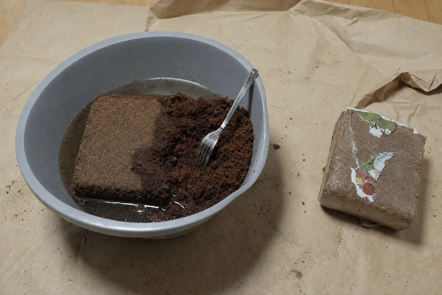Ett halvt upplöst kokosfiberblock i en balja med vatten, bredvid ligger ett torrt pressat block